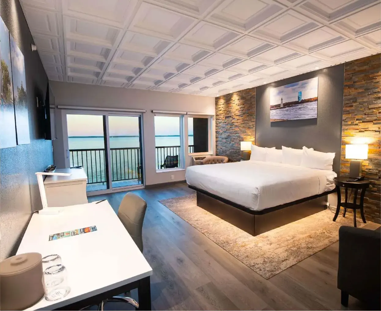 Ein Kingsize-Bett mit weißem Bettzeug vor einer strukturierten Steinwand, die von zwei Nachttischlampen beleuchtet wird.