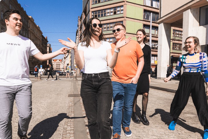 Eine Gruppe von fünf jungen Erwachsenen, die an einem sonnigen Tag lächelnd auf einer Straße in der Stadt spazieren gehen und sich dabei unterhalten.