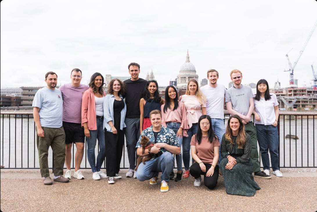 Group of diverse young adults standing outdoors in front of a cityscape with a historic dome, some smiling and one person holding a small do