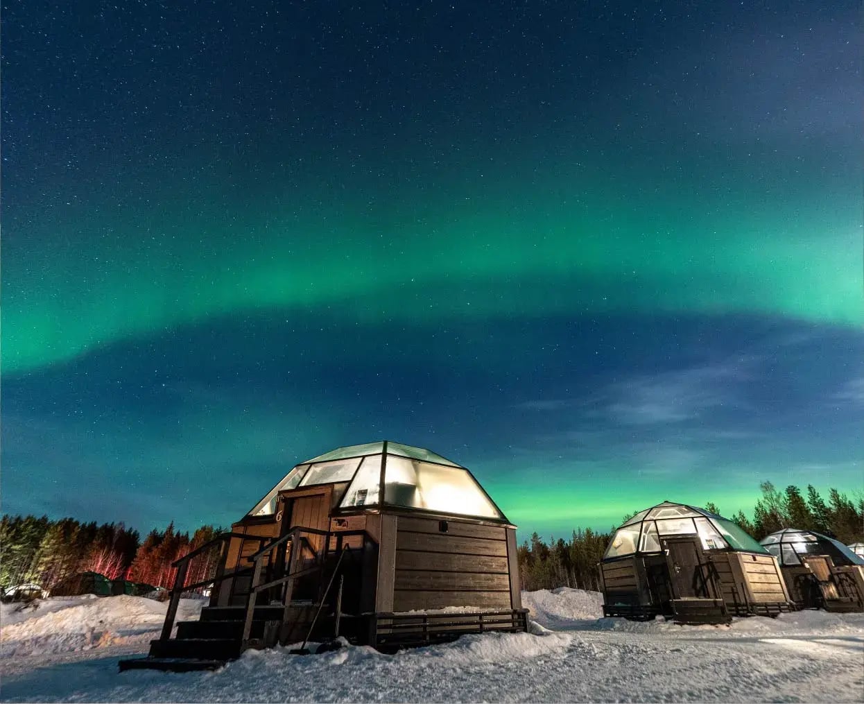 Glass-sided cabins under the Northern Lights in a snowy landscape at night.