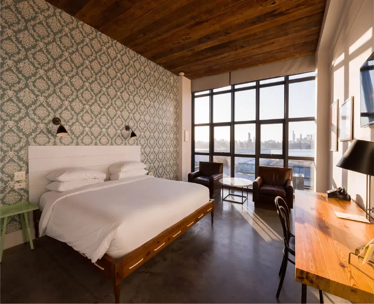 Large window with city skyline view, two brown armchairs, and a wooden desk with a black chair.