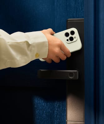 Hand holding a smartphone near a digital door lock on a blue door.