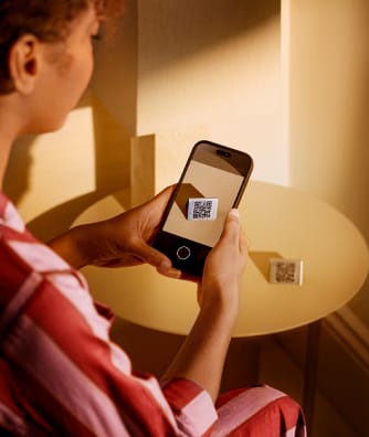 Eine Person scannt einen QR-Code auf dem Bildschirm eines Smartphones und einen zweiten QR-Code an der Wand in der Nähe.