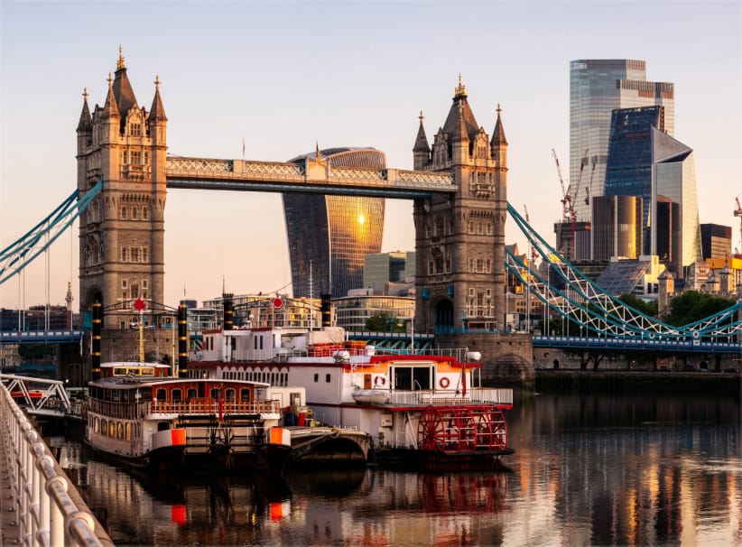 Tower Bridge over the River Thames with modern skyscrapers in the background during sunset.
